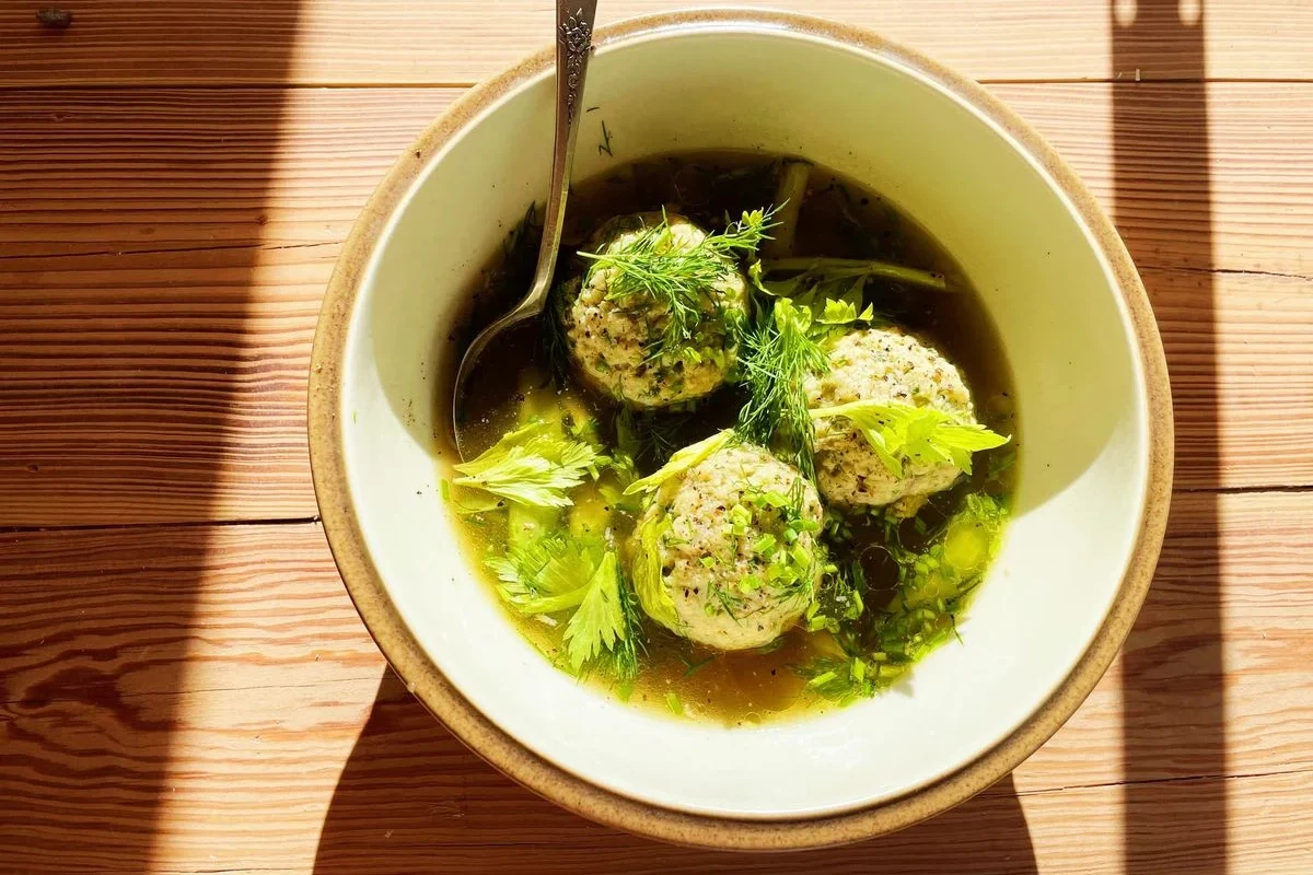 A steaming bowl of clear golden chicken broth with a single, light, fluffy matzo ball and fresh dill garnish.