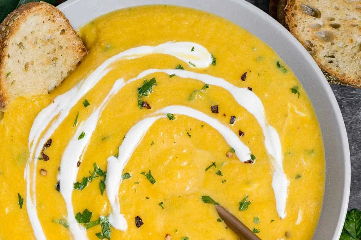 A bowl of creamy orange butternut squash leek soup topped with fresh herbs and a drizzle of olive oil.