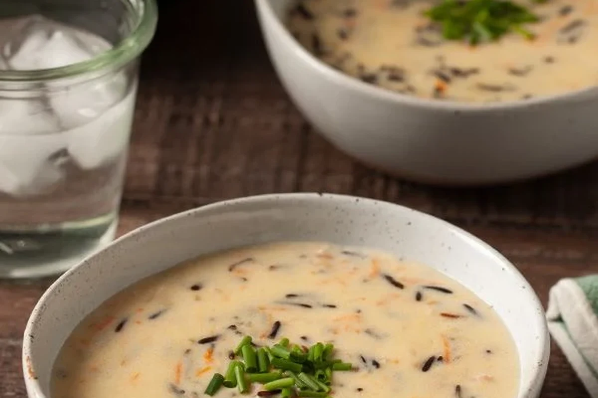 Byerlys Wild Rice Soup Recipe – Creamy Chicken Soup Copycat 2 A steaming bowl of creamy wild rice soup with chicken, carrots, and herbs, served in a rustic kitchen setting.