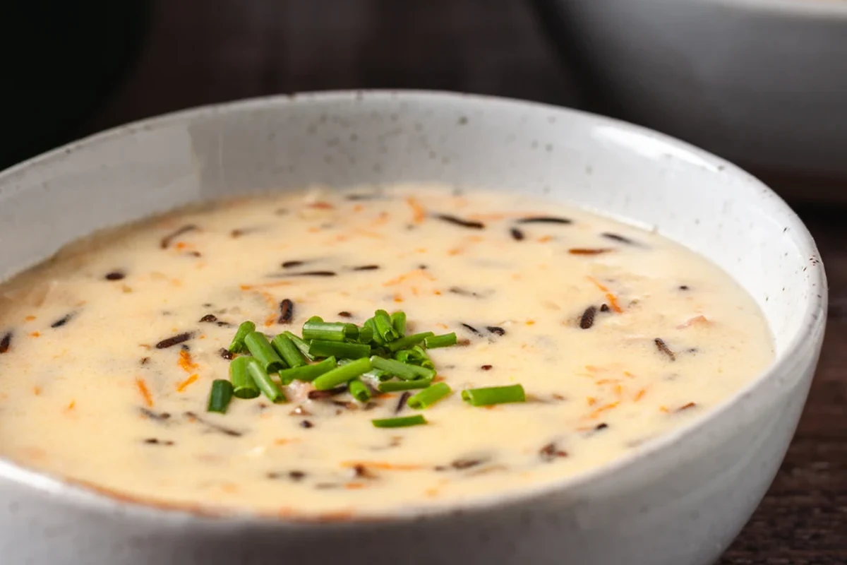 Byerlys Wild Rice Soup Recipe – Creamy Chicken Soup Copycat 3 A steaming bowl of creamy wild rice soup with chicken, carrots, and herbs, served in a rustic kitchen setting.