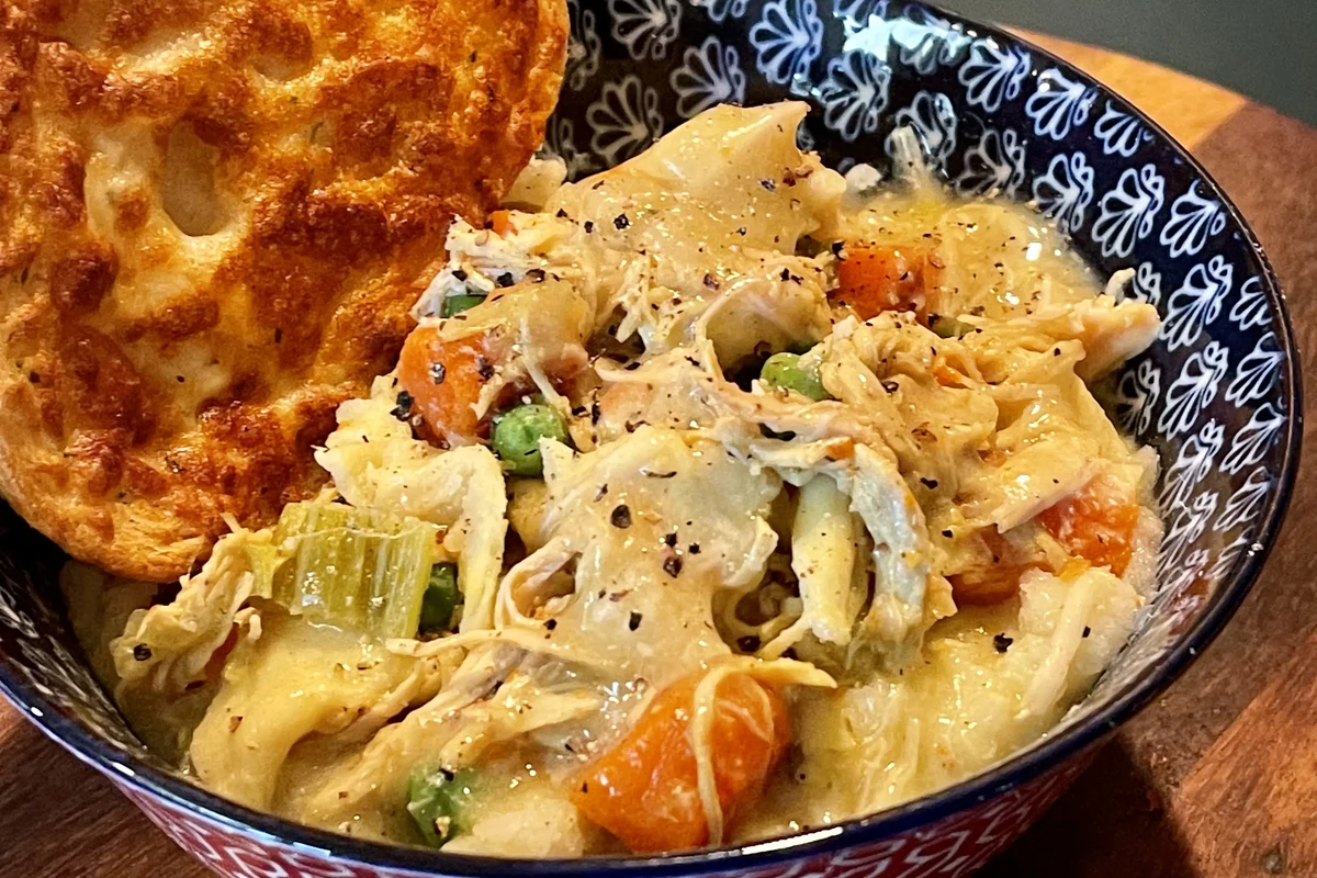 A hearty bowl featuring creamy mashed potatoes topped with savory chicken noodle soup and fresh herbs.