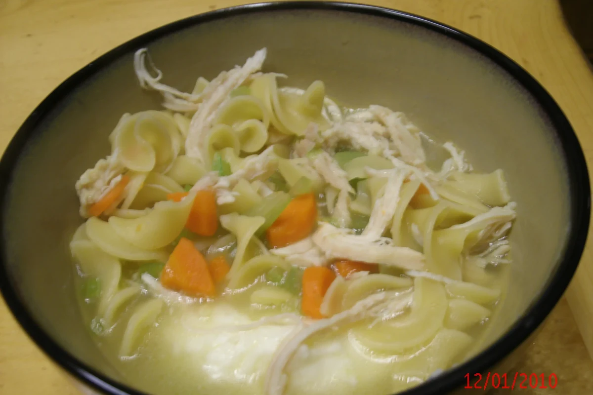 A hearty bowl featuring creamy mashed potatoes topped with savory chicken noodle soup and fresh herbs.