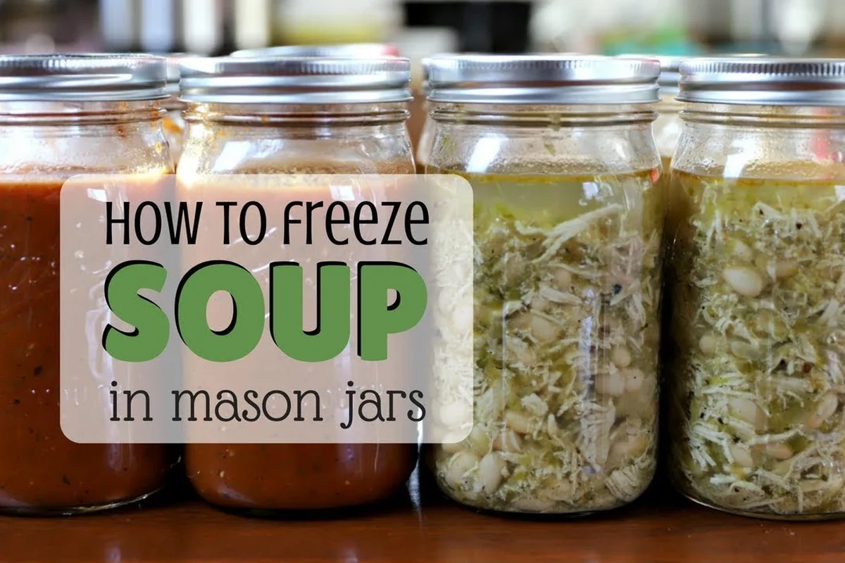 A row of straight-sided glass Mason jars filled with homemade soup stored neatly in a freezer.