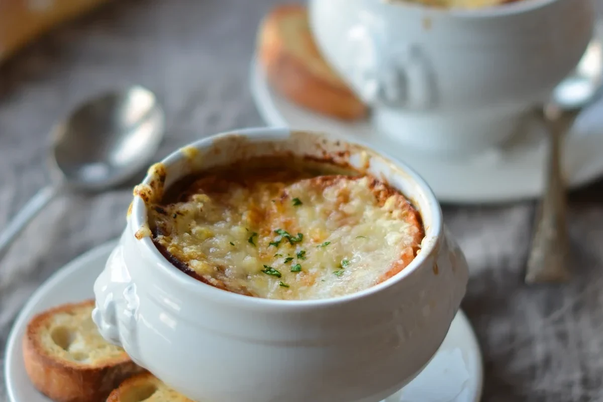 A steaming bowl of traditional French onion soup, or soupe à l’oignon, topped with a golden, melted Gruyère crust and a slice