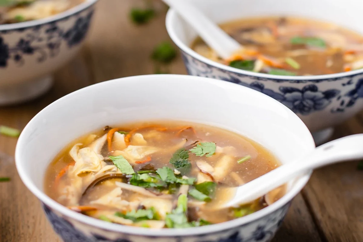 A steaming bowl of homemade hot and sour soup with visible egg ribbons, tofu, and wood ear mushrooms.