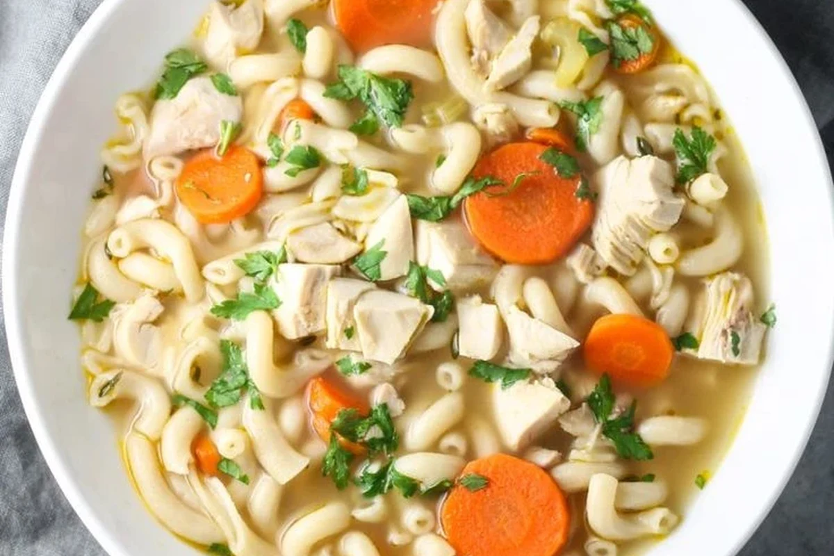 Low FODMAP Chicken Noodle Soup Recipe for Sensitive Stomachs 3 A steaming bowl of homemade chicken noodle soup with fresh herbs and carrots on a rustic wooden table.