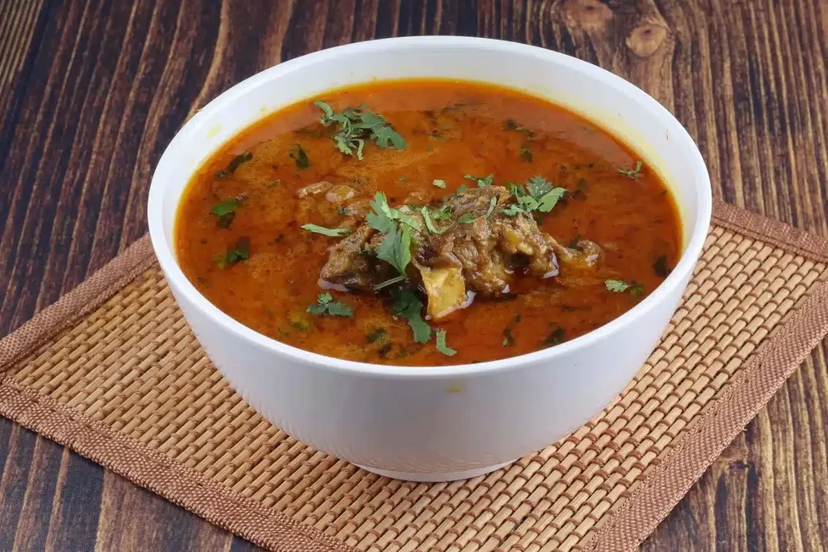 A steaming bowl of traditional Belizean mutton soup with root vegetables and dumplings.