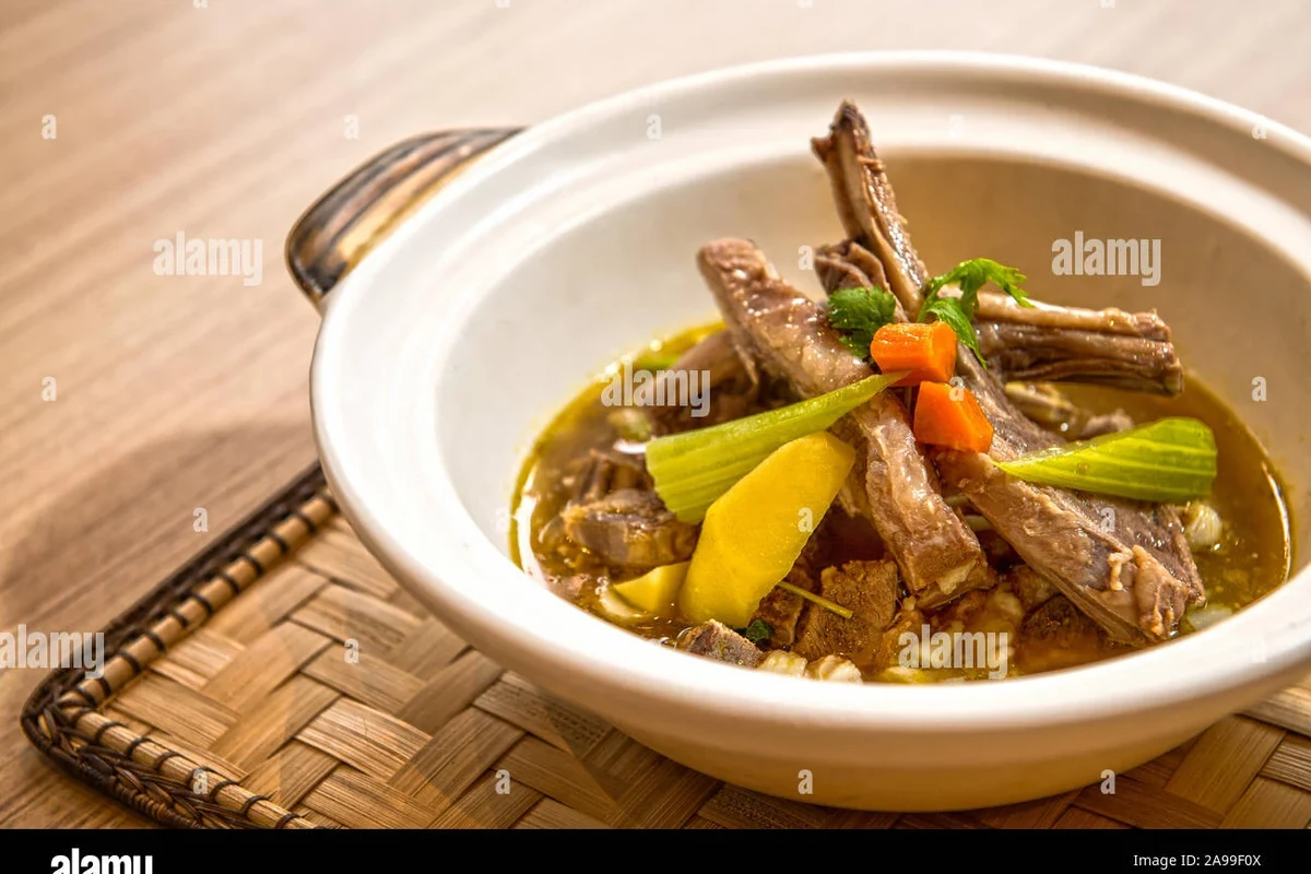 A steaming bowl of traditional Belizean mutton soup with root vegetables and dumplings.