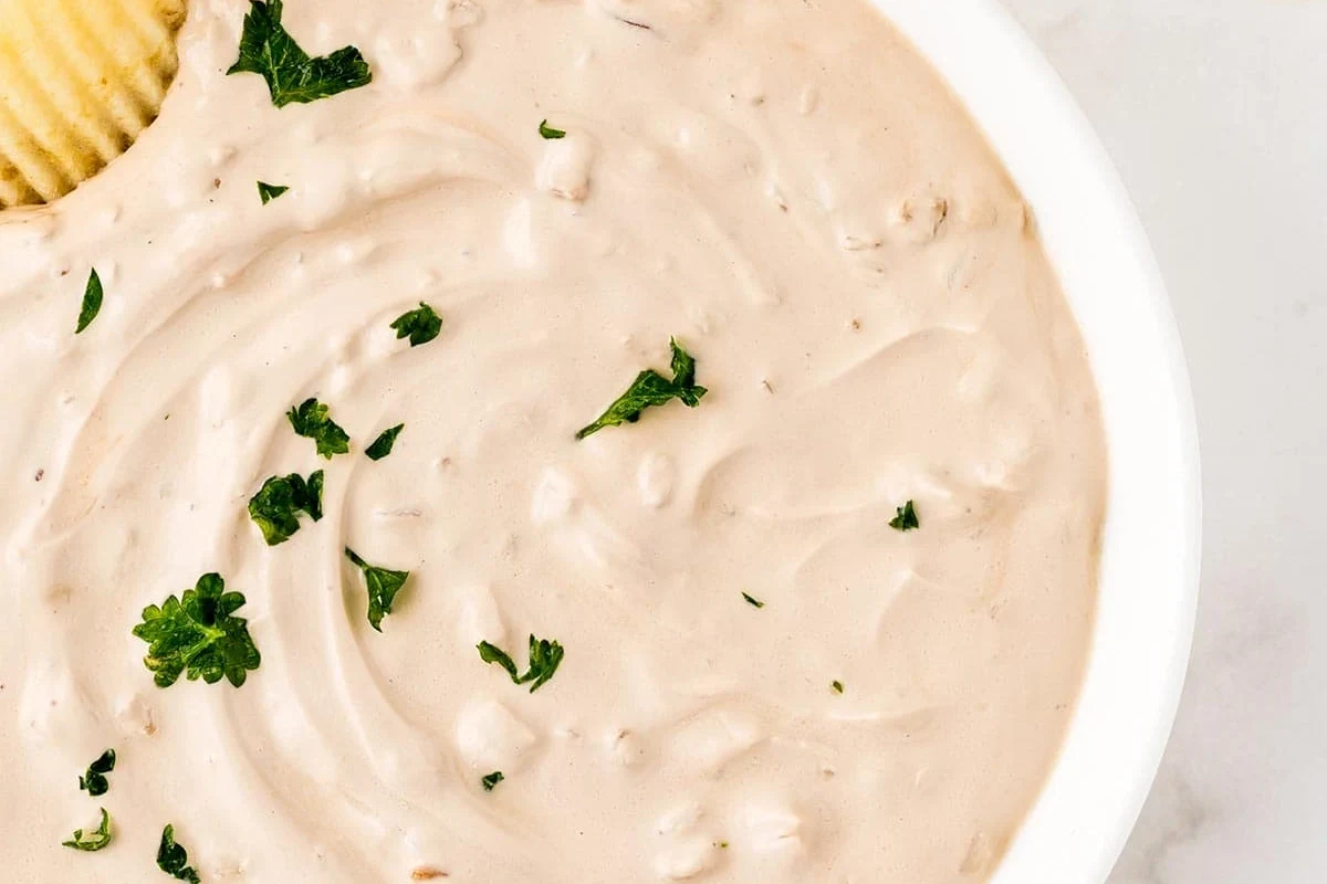 Onion Dip with Onion Soup Mix: Easy Creamy Party Recipe 3 A bowl of creamy onion dip served with potato chips on a wooden table.