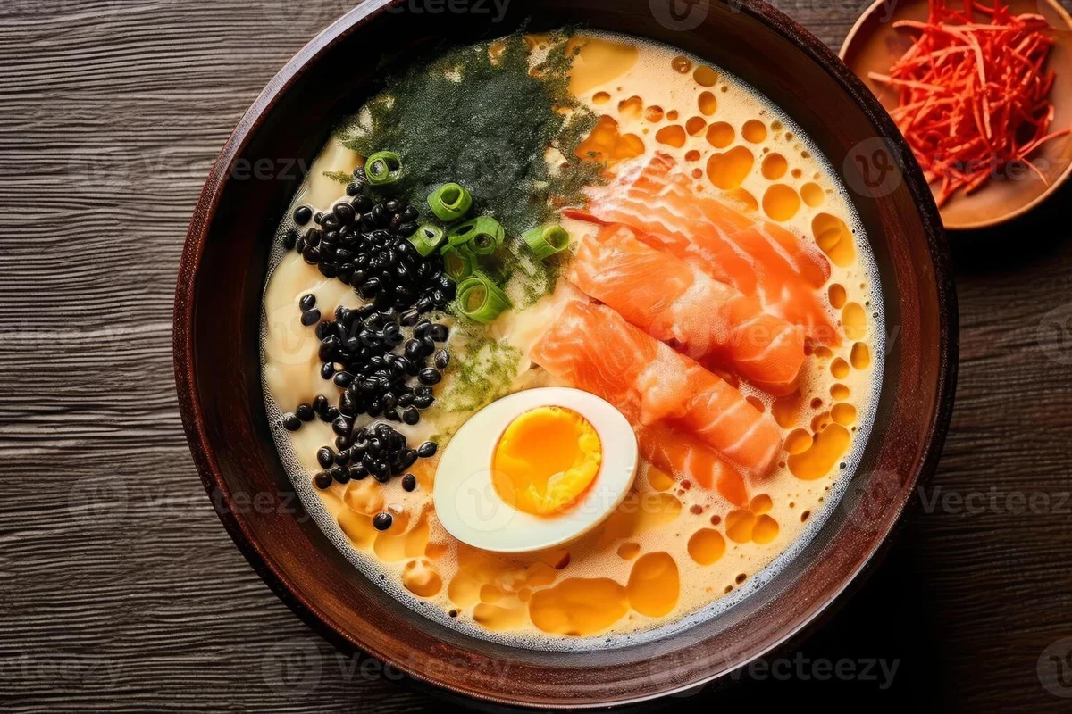 Japanese Soup Stock (Dashi): Authentic Recipe, Ingredients & Uses 2 A bowl of clear Japanese dashi stock with dried kombu and bonito flakes beside it on a wooden table.