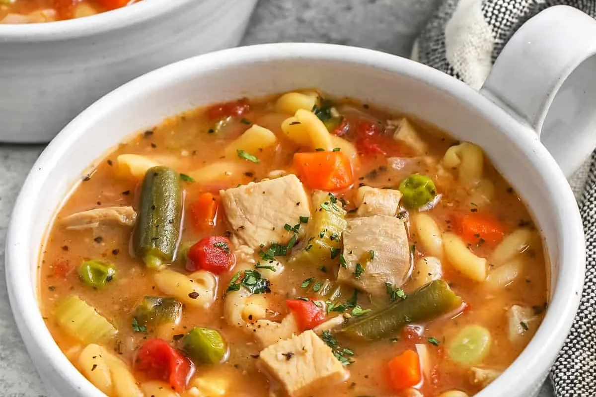 A steaming bowl of homemade turkey soup with vegetables and fresh herbs on a rustic kitchen table.