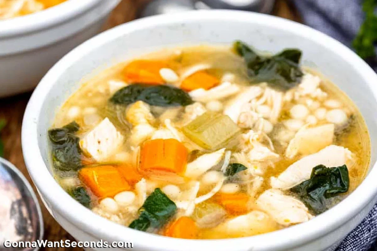 A steaming bowl of homemade turkey soup with vegetables and fresh herbs on a rustic kitchen table.