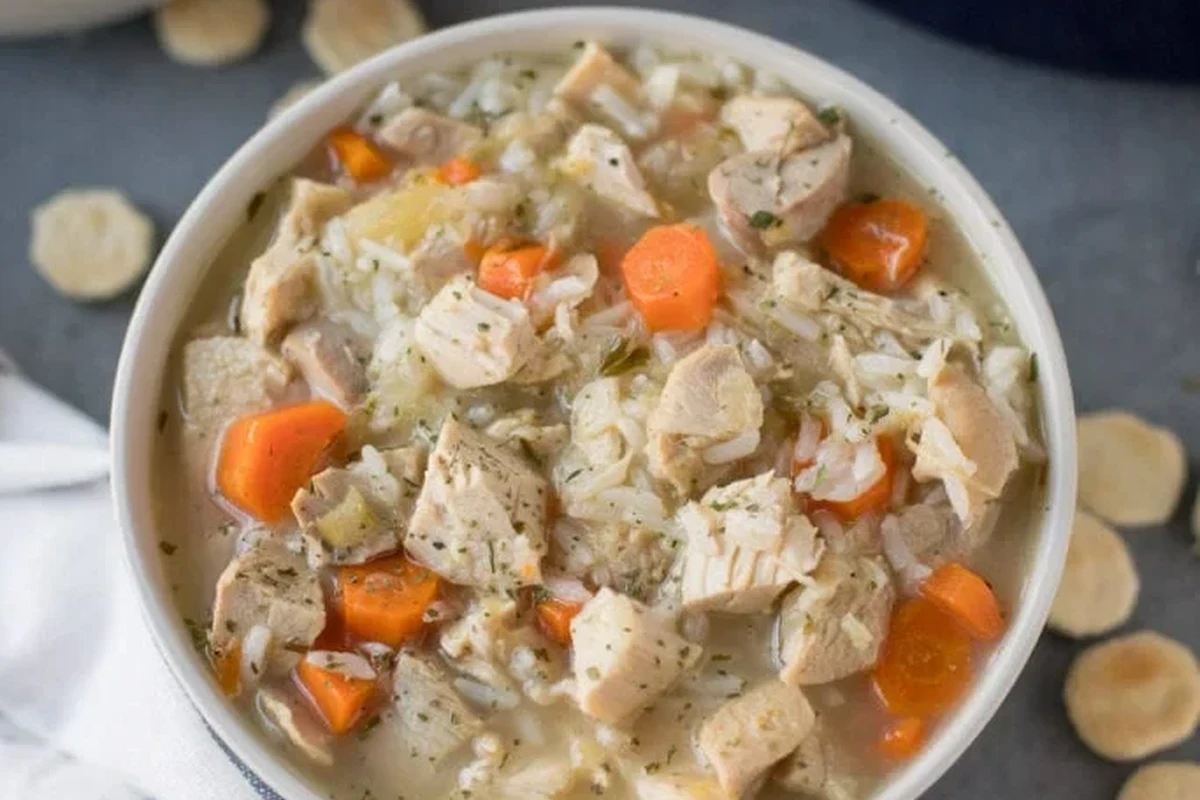 A steaming bowl of homemade turkey soup with vegetables and fresh herbs on a rustic kitchen table.