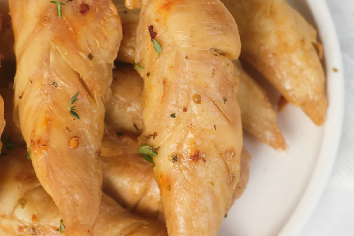 A pot of chicken tenders simmering in broth with fresh herbs and aromatics.