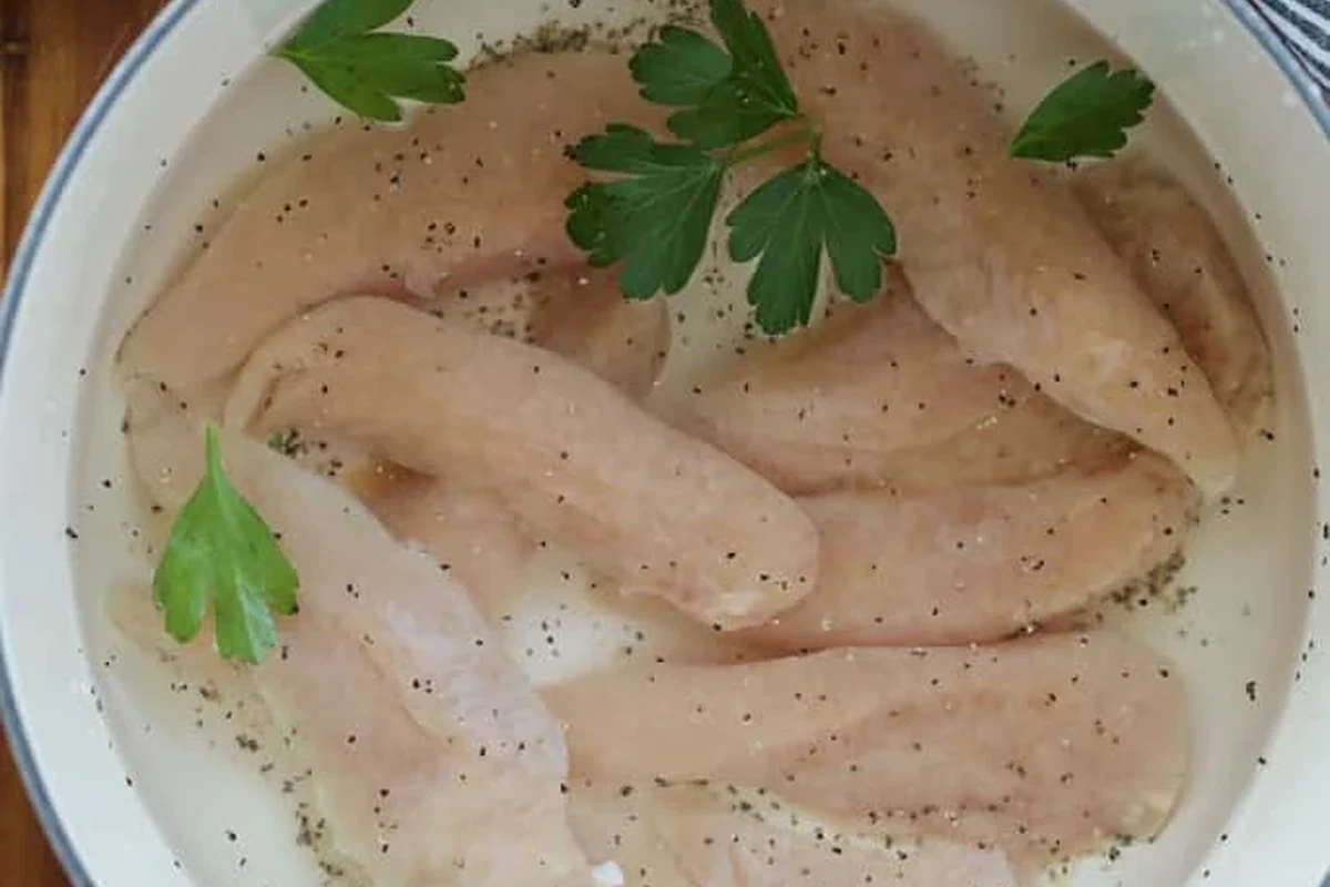 A pot of gently simmering chicken tenders with fresh herbs and aromatics in a kitchen setting.