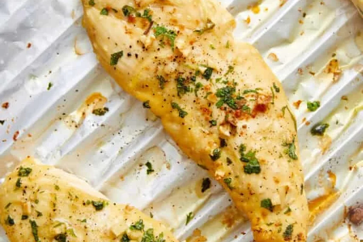 A perfectly golden-brown broiled chicken breast on a plate with fresh herbs.