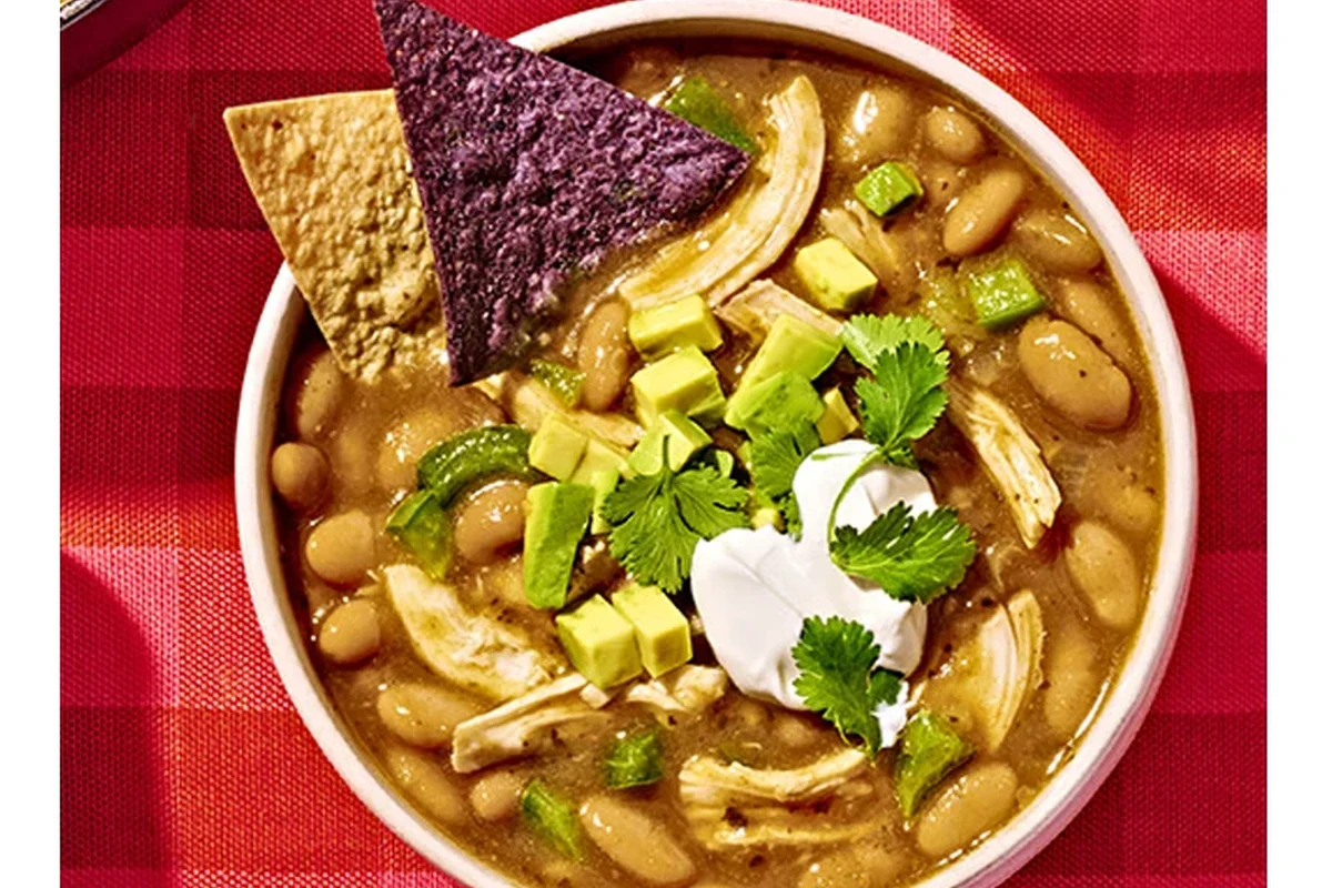 A warm, hearty bowl of white chicken chili topped with fresh cilantro, shredded cheese, and lime wedges.