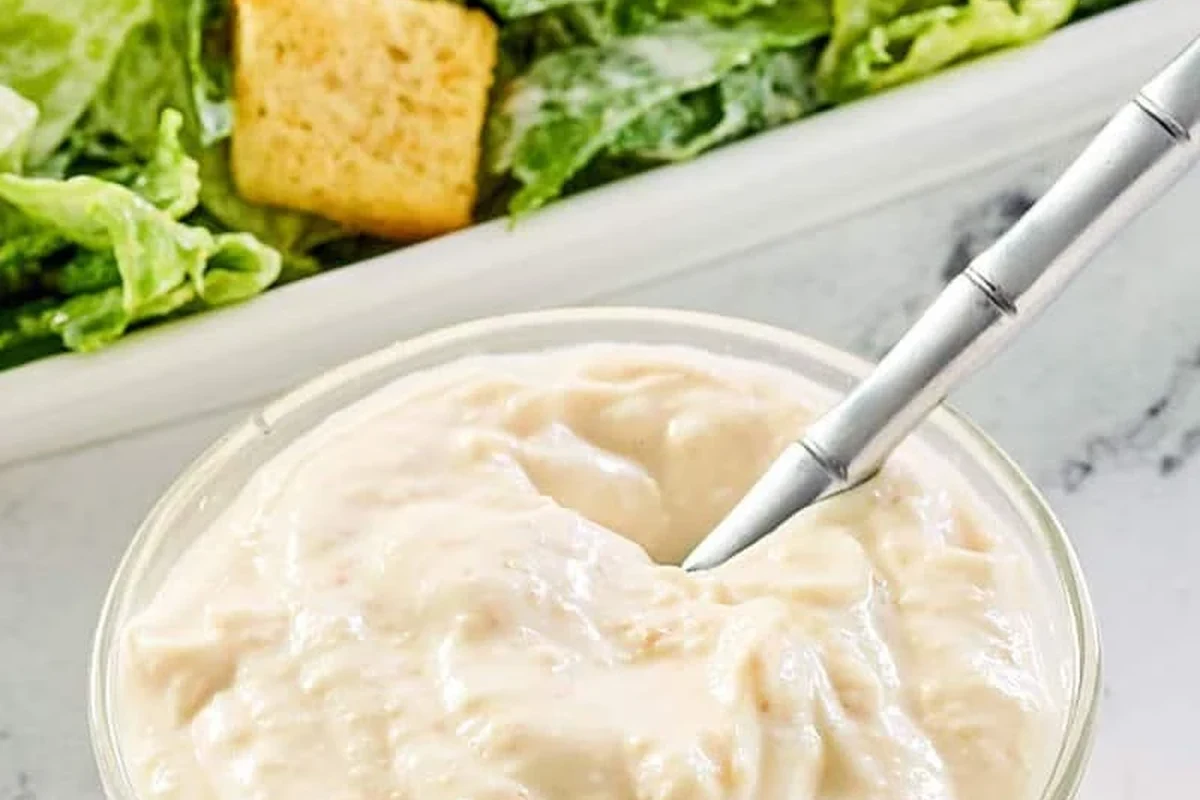 A bowl of creamy homemade Caesar dressing garnished with fresh Parmesan and black pepper.
