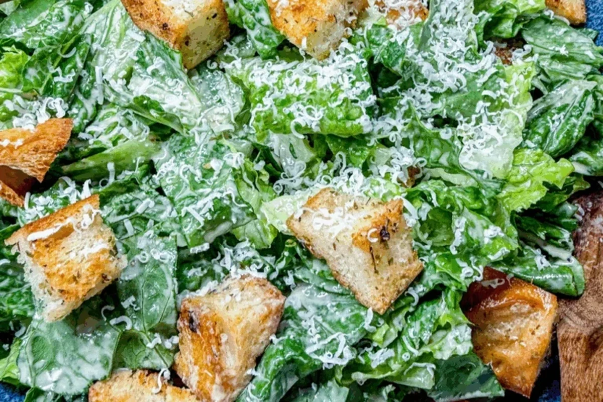 A glass bowl filled with creamy homemade Caesar dressing, drizzled with olive oil and topped with fresh parmesan cheese.