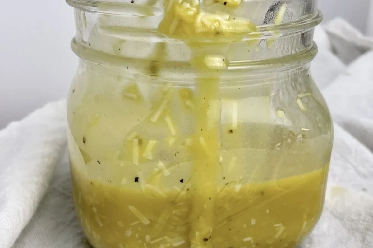 Caesar Dressing Without Mayo 2 A bowl of fresh, creamy homemade Caesar dressing without mayo beside fresh ingredients like lemon, garlic, and herbs.