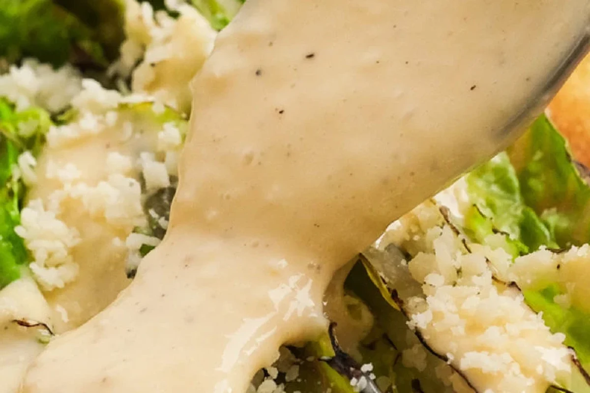A glass bowl filled with creamy homemade Caesar dressing, whisked to perfection with fresh ingredients on a wooden kitchen co