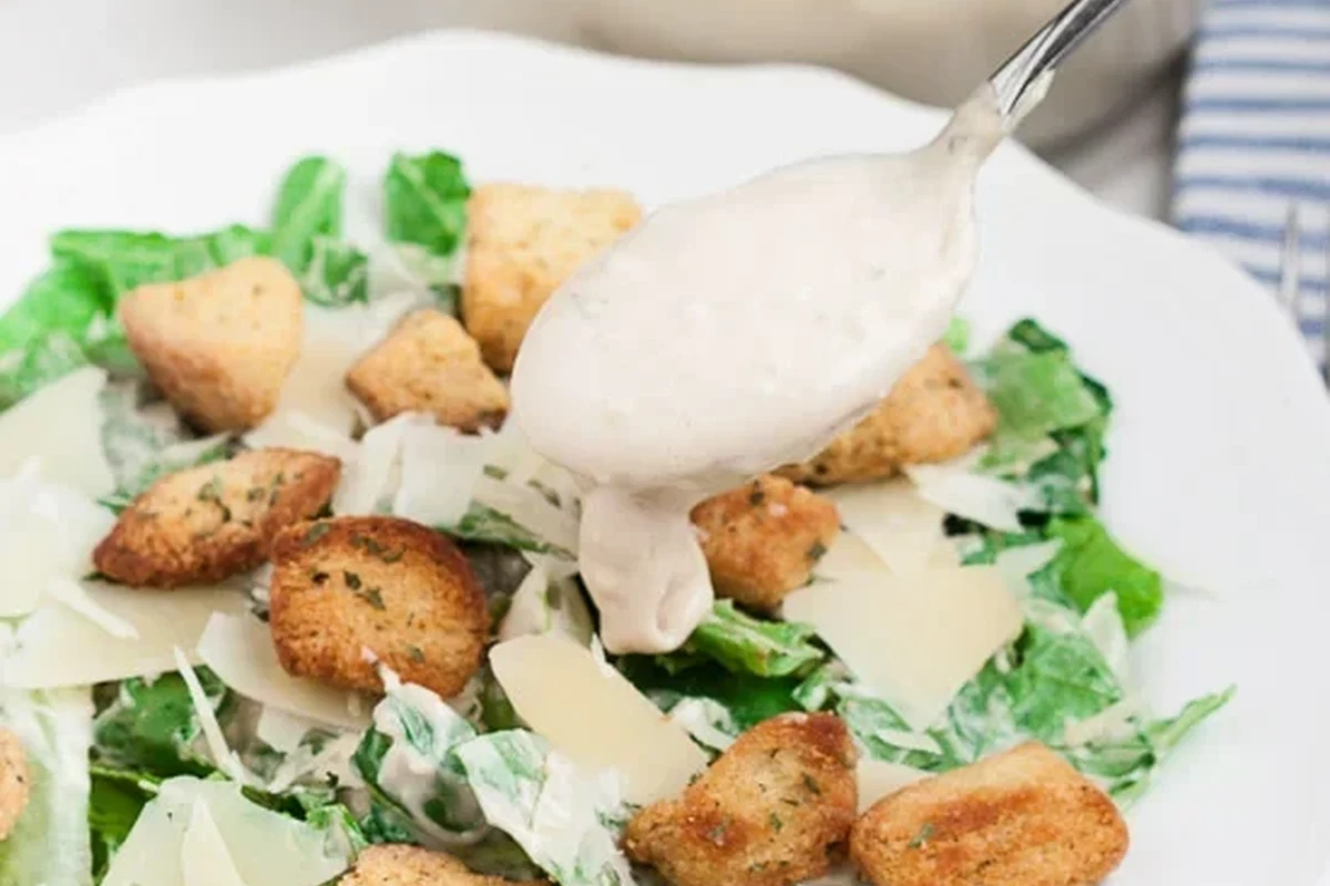 A glass bowl filled with creamy homemade Caesar dressing, whisked to perfection with fresh ingredients on a wooden kitchen co