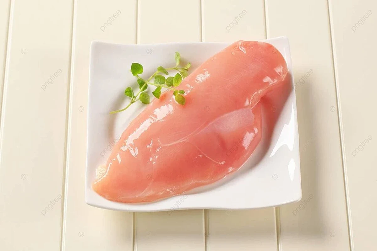 Fresh raw chicken fillet breasts prepped for cooking on a wooden cutting board with lime and herbs.