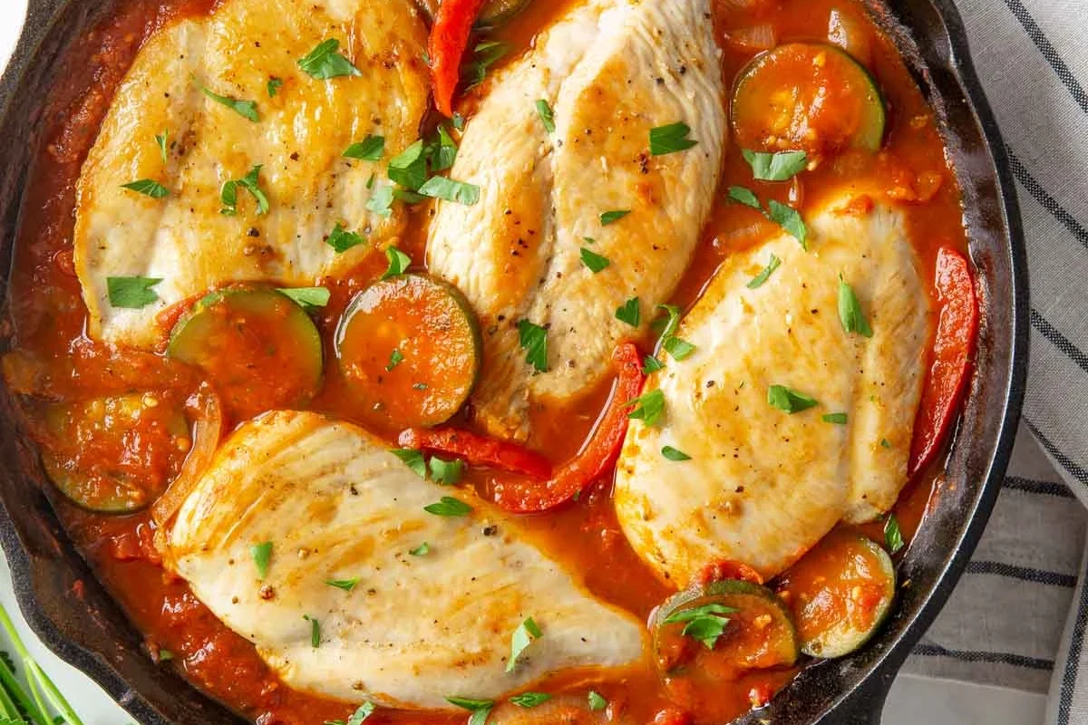A skillet of golden-brown chicken simmering in a rich tomato sauce with fresh basil and melted mozzarella cheese.