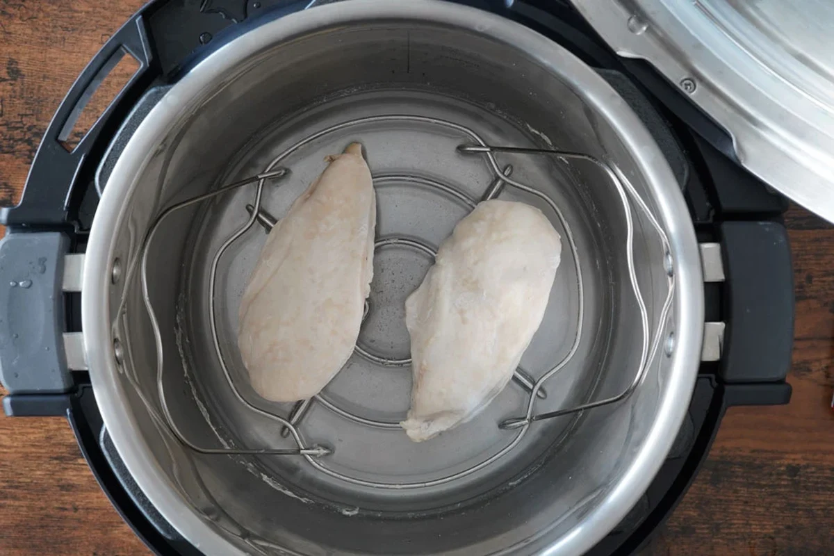 A stainless steel Instant Pot containing cooked chicken breast on a trivet with steam rising.