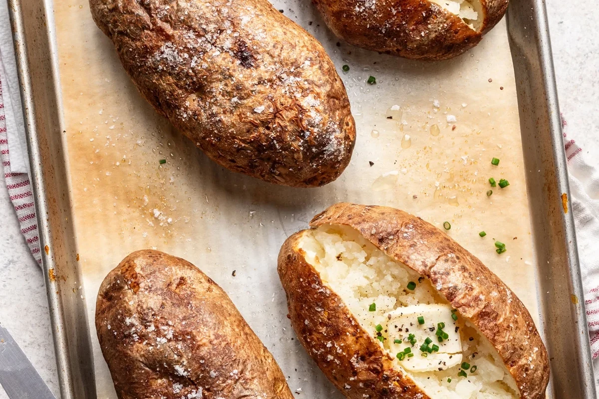 A perfectly baked Russet potato with a golden, crispy skin served on a rustic plate.