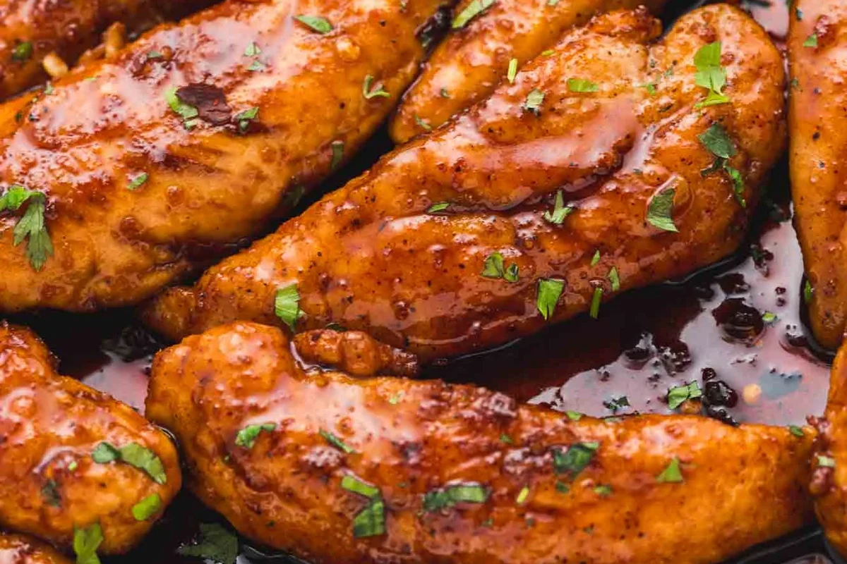 A platter of golden-brown crispy chicken tenders served with lime wedges and fresh herbs.