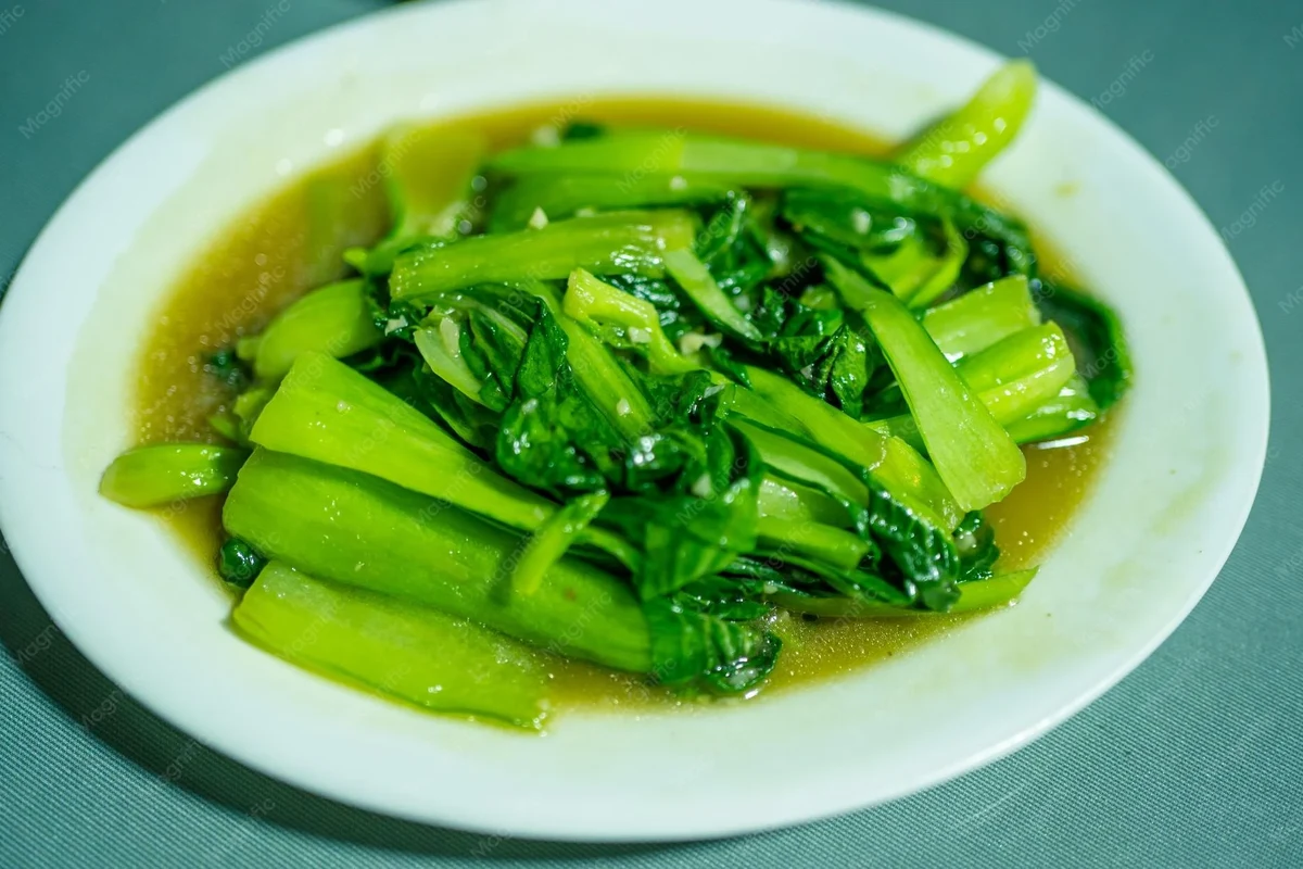 Fresh assortment of green vegetables and herbs including chayote, cilantro, and chaya leaves on a wooden kitchen surface.