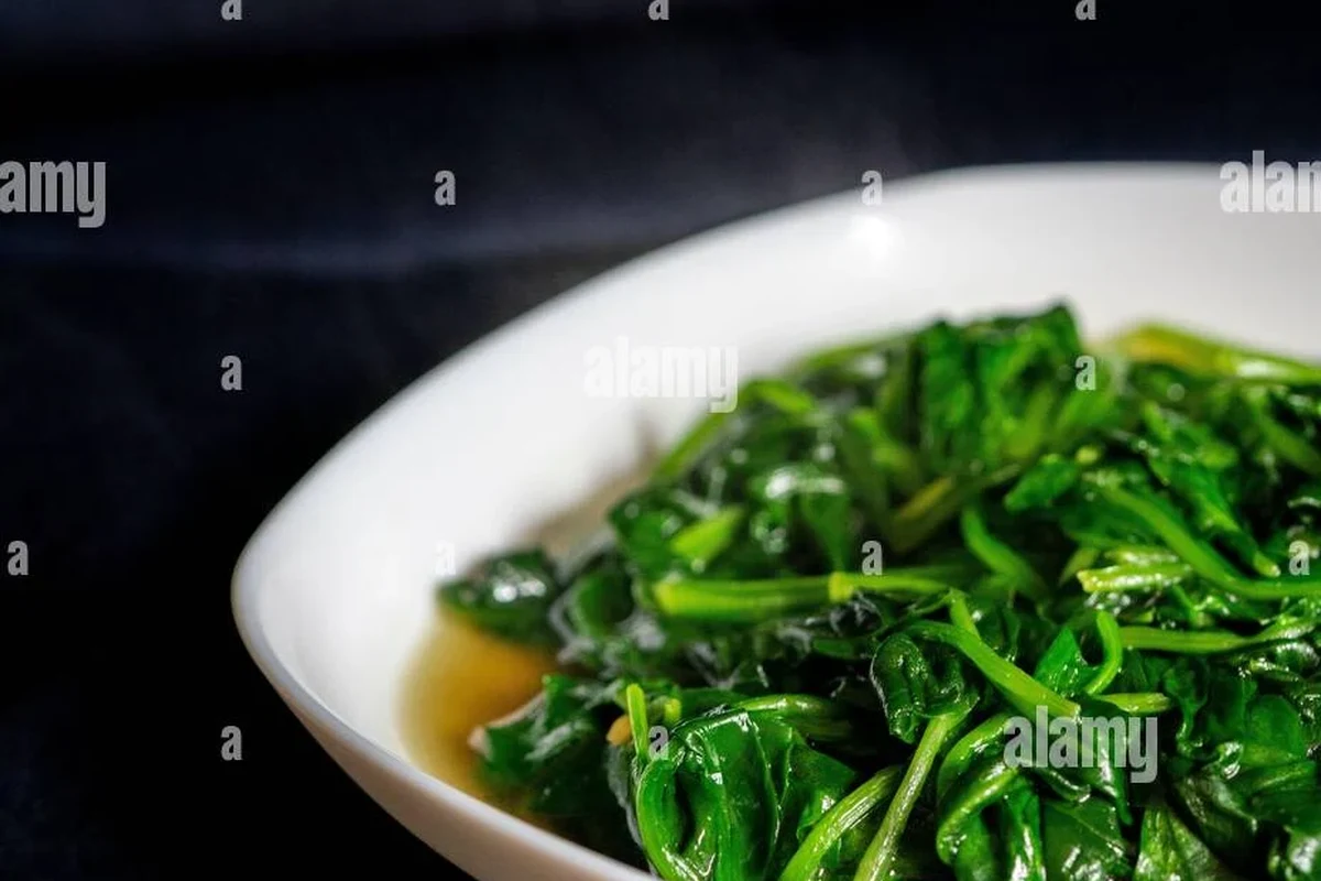 Fresh assortment of green vegetables and herbs including chayote, cilantro, and chaya leaves on a wooden kitchen surface.