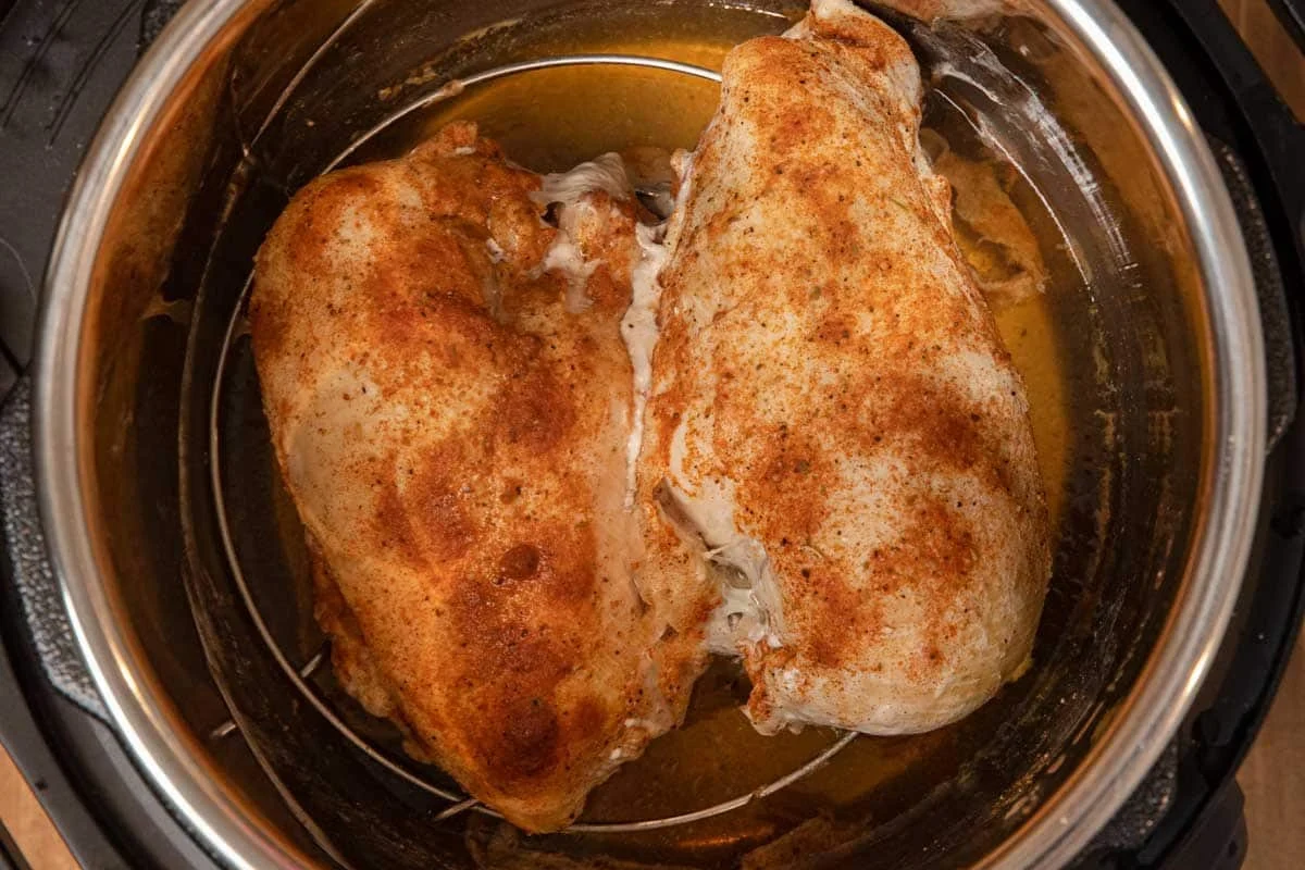 Succulent pressure-cooked chicken breast with fresh herbs and a side of broth in a modern kitchen.