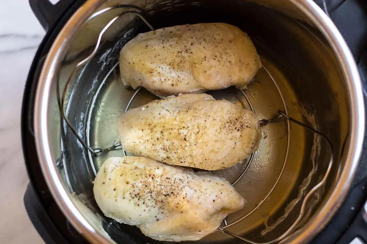 A stainless steel pressure cooker with cooked, tender chicken breasts inside, garnished with fresh herbs.
