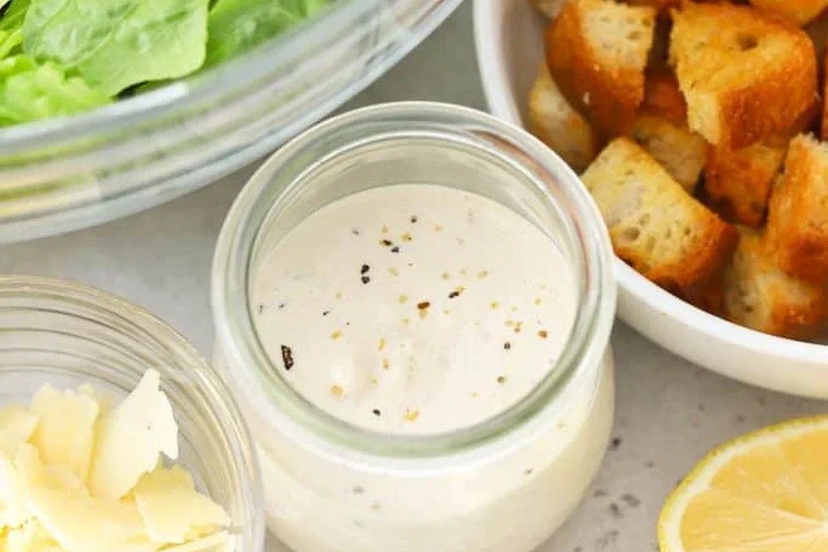 Gluten Free Caesar Dressing 2 A bowl of creamy homemade Caesar dressing with fresh garlic, lemon, and parmesan cheese on a kitchen table.