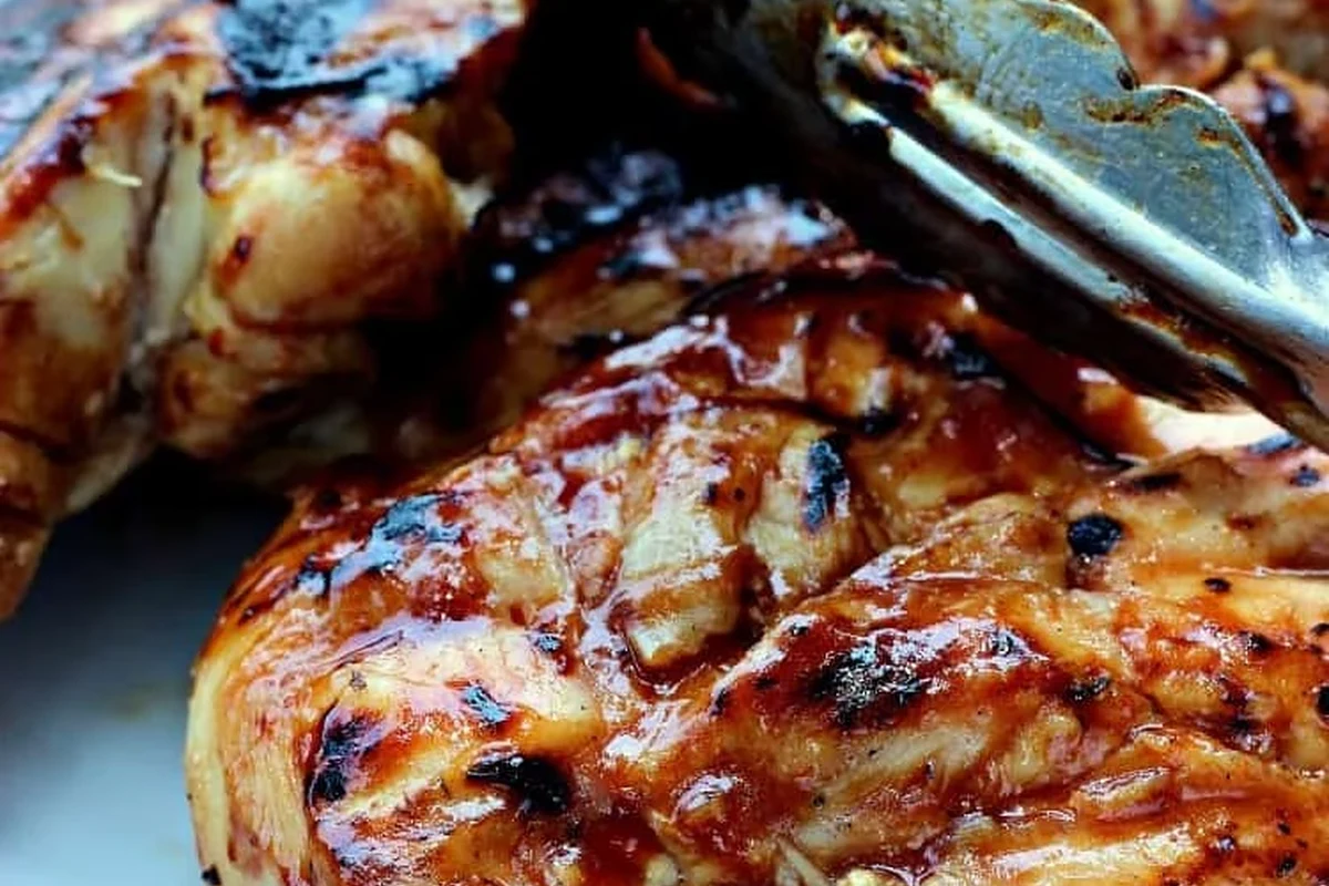 Golden brown grilled chicken breast cooking over hot charcoal on a backyard grill