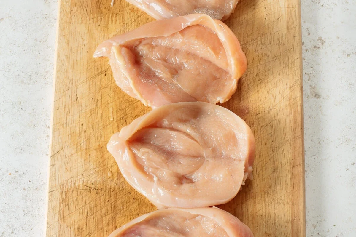 Fresh raw halved chicken breasts seasoned with spices on a wooden cutting board ready for cooking.