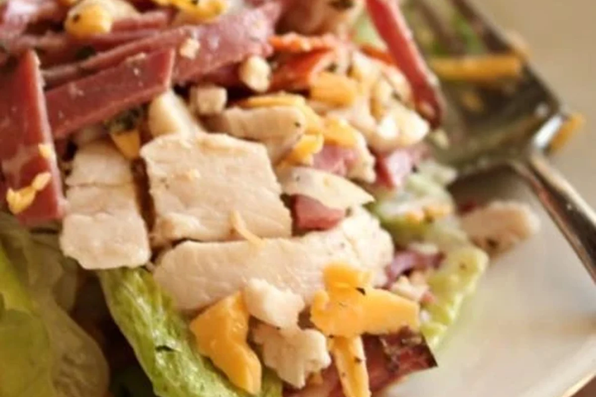 A vibrant hoagie salad in a white bowl with salami, provolone, peppers, and greens.