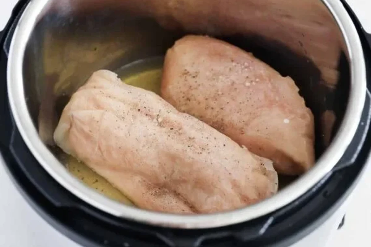 Tender, cooked chicken breasts prepared in an Instant Pot, seasoned with spices on a wooden cutting board.