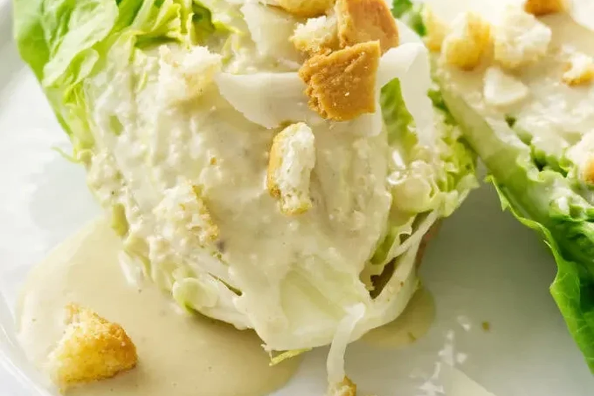 A bowl of homemade light Caesar dressing next to fresh romaine lettuce and lemon wedges.