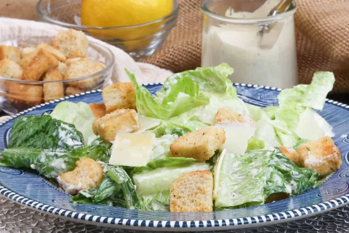 A bowl of homemade light Caesar dressing next to fresh romaine lettuce and lemon wedges.