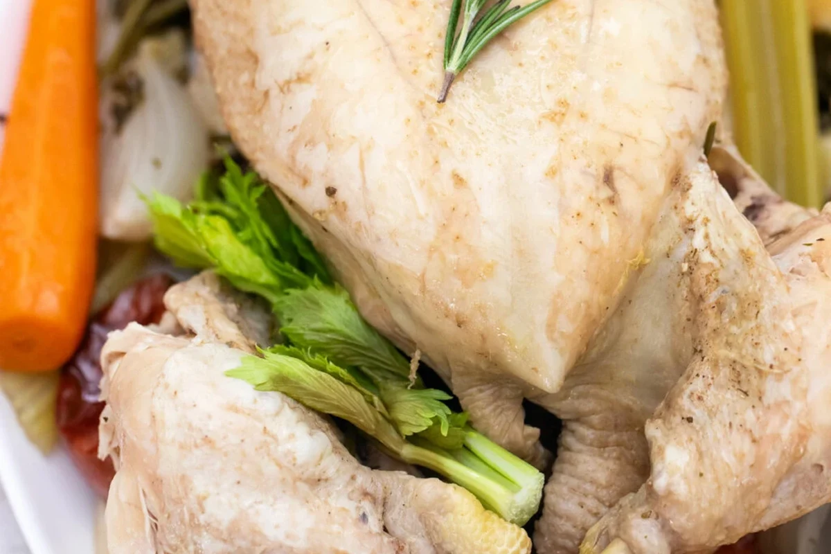 A whole chicken simmering in a large pot with fresh vegetables and herbs for broth.