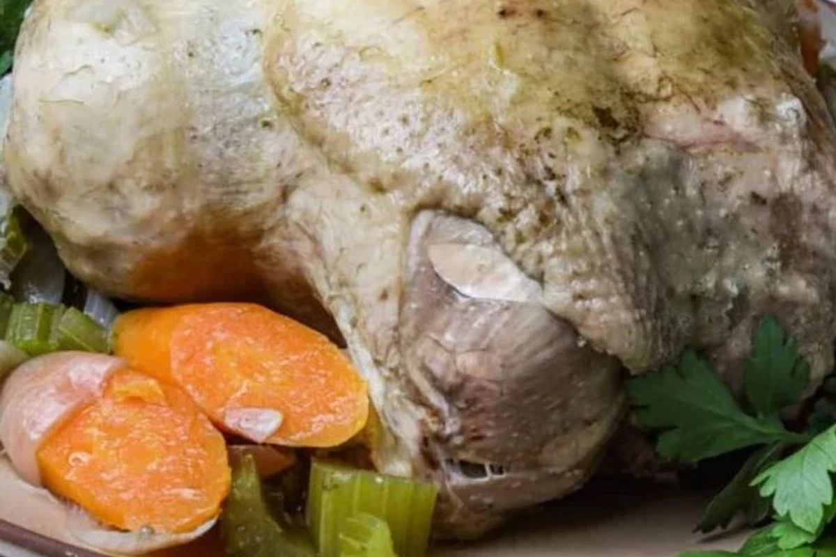 A whole chicken simmering in a large pot with fresh vegetables and herbs for broth.