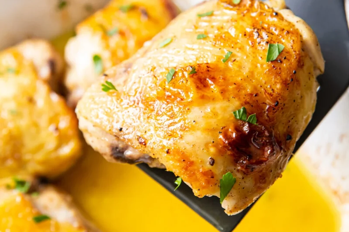 Golden brown broiled chicken thighs served on a platter with fresh herbs.