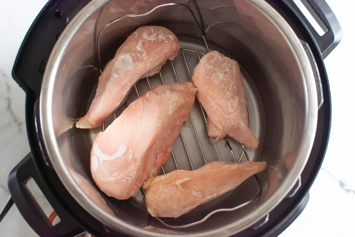 A stainless steel Instant Pot containing cooked chicken breasts with fresh herbs on a wooden kitchen counter.