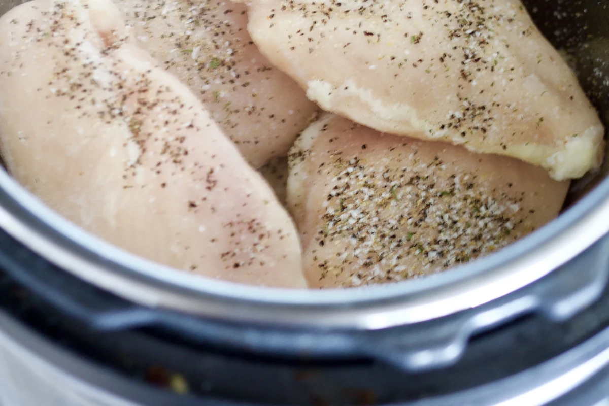 How Long to Cook Frozen Chicken Breast in Instant Pot 2 A cooked, juicy chicken breast on a plate next to an Instant Pot in a bright kitchen.