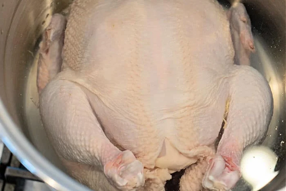 A whole chicken simmering in a large stockpot with aromatics like onion and garlic for a flavorful broth.