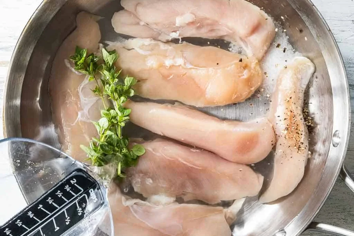 A pot of water with chicken tenders simmering gently on a stove for meal prep.