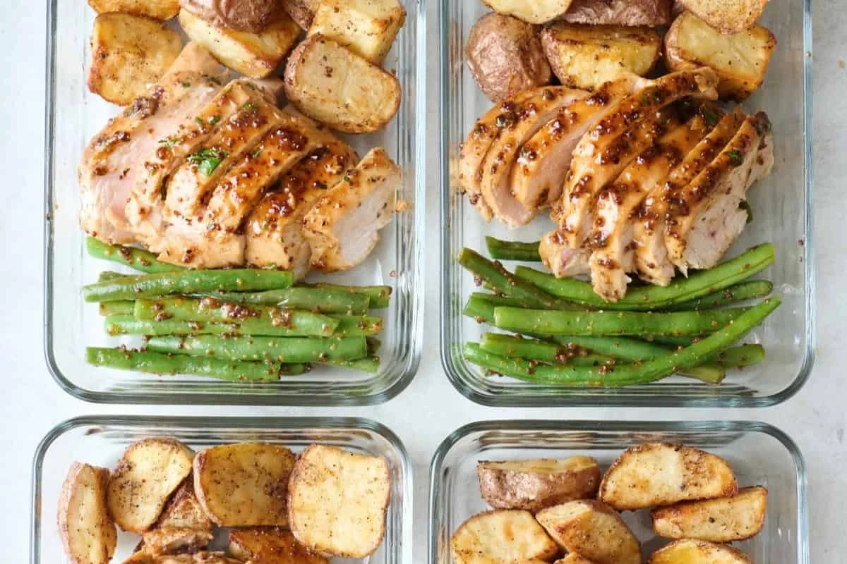A variety of meal-prepped glass containers filled with roasted chicken breast, fresh vegetables, and grains.